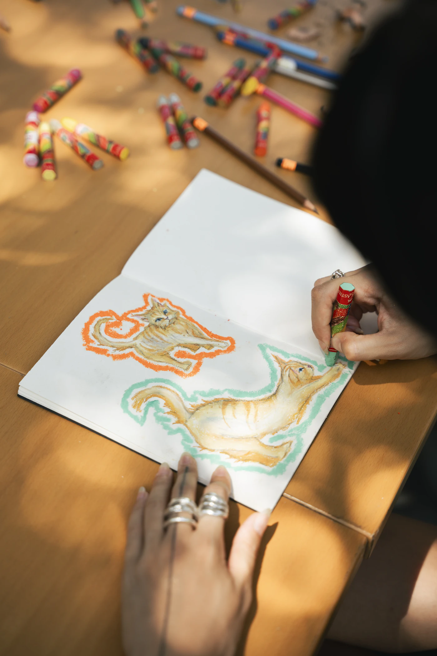 Hands drawing colorful cats with crayons in a sketchbook