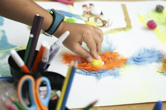 Child's hand creating art with colorful feathers and markers.