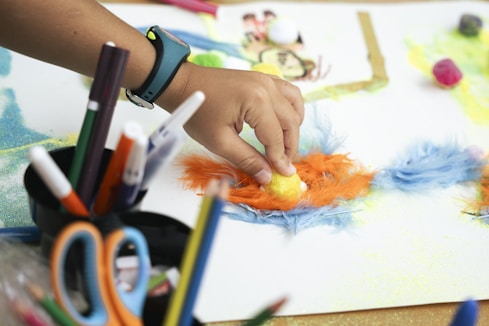 Child's hand creating art with colorful feathers and markers.