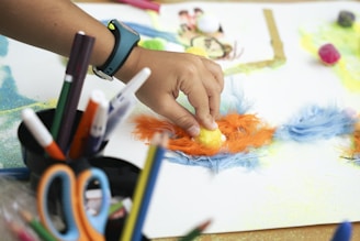 Child's hand creating art with colorful feathers and markers.