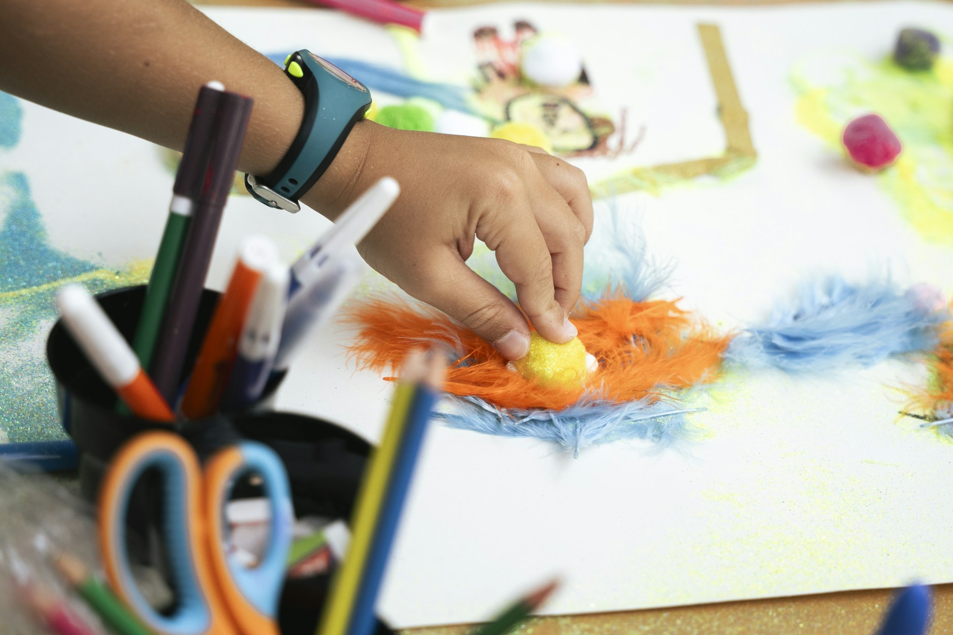 Child's hand creating art with colorful feathers and markers.