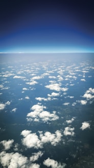 Fluffy clouds float above land seen from above.