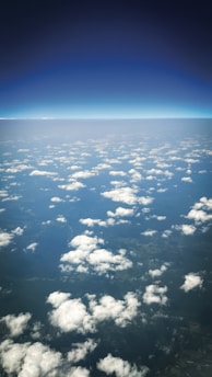 Fluffy clouds float above land seen from above.