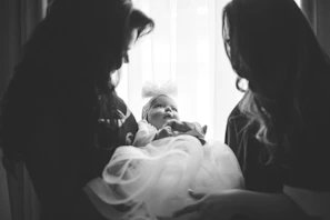 Two women hold a baby dressed in white