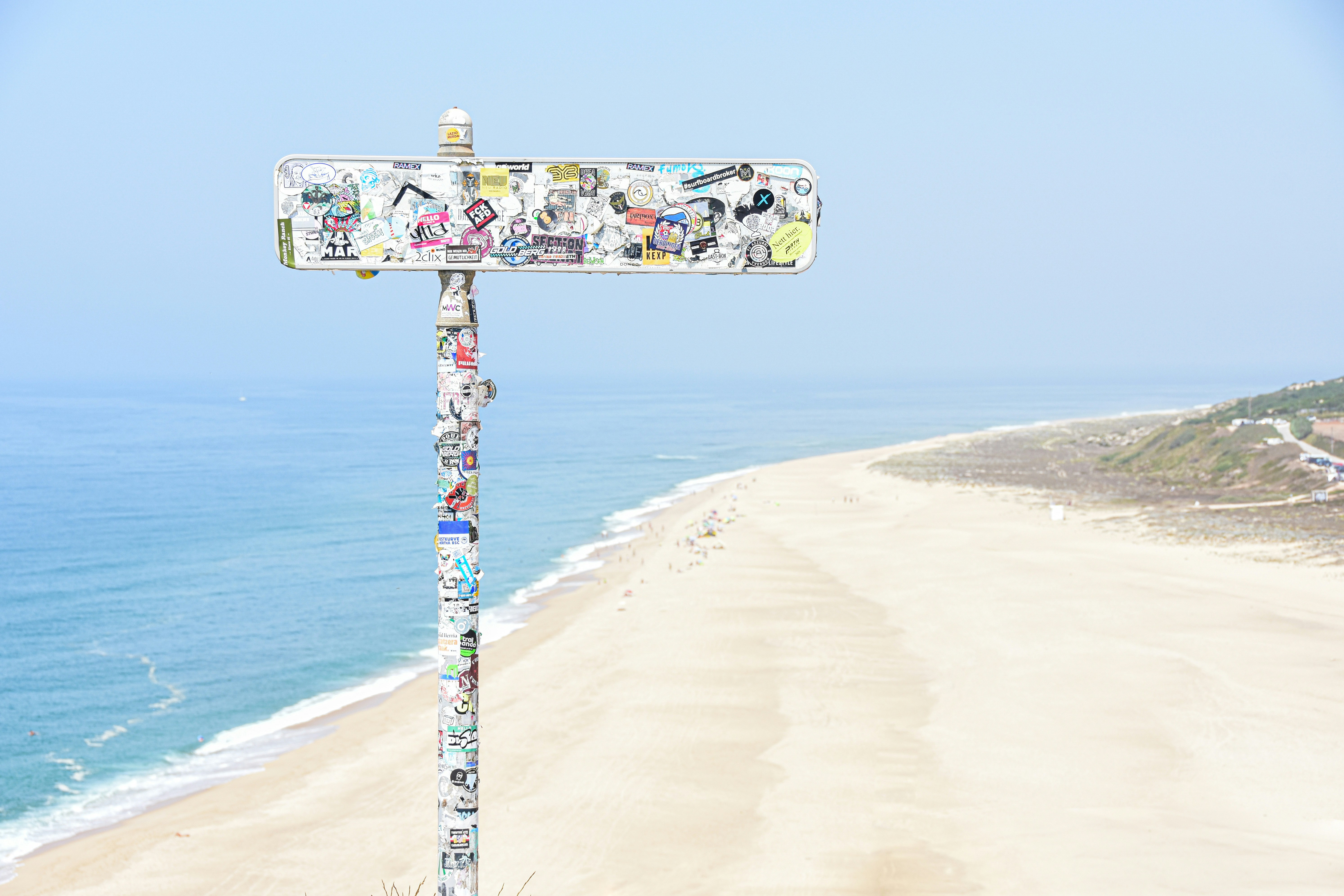 Signpost covered in stickers on a sandy beach