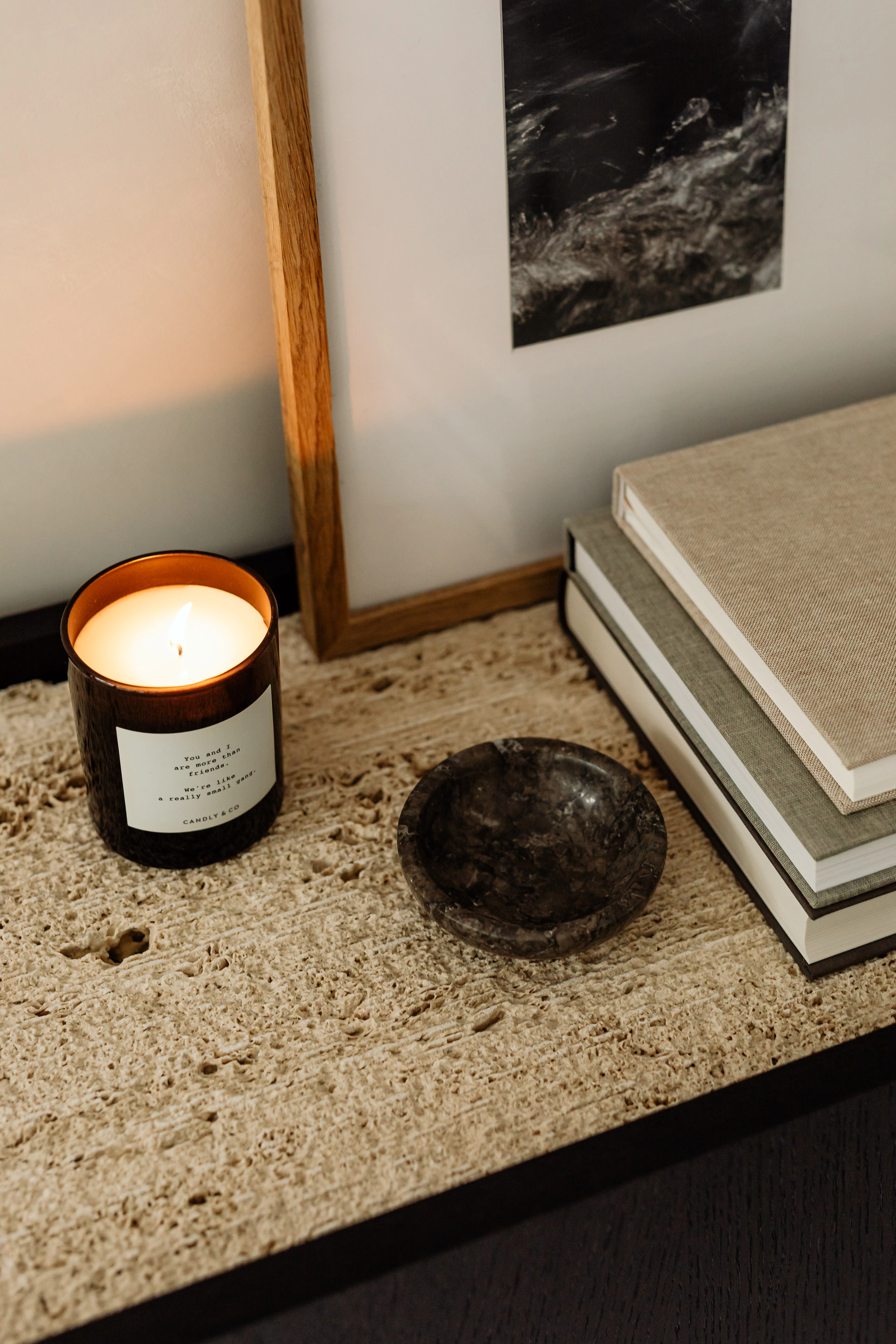 Lit candle, dark stone dish and linen-bound books on a textured sand-coloured surface