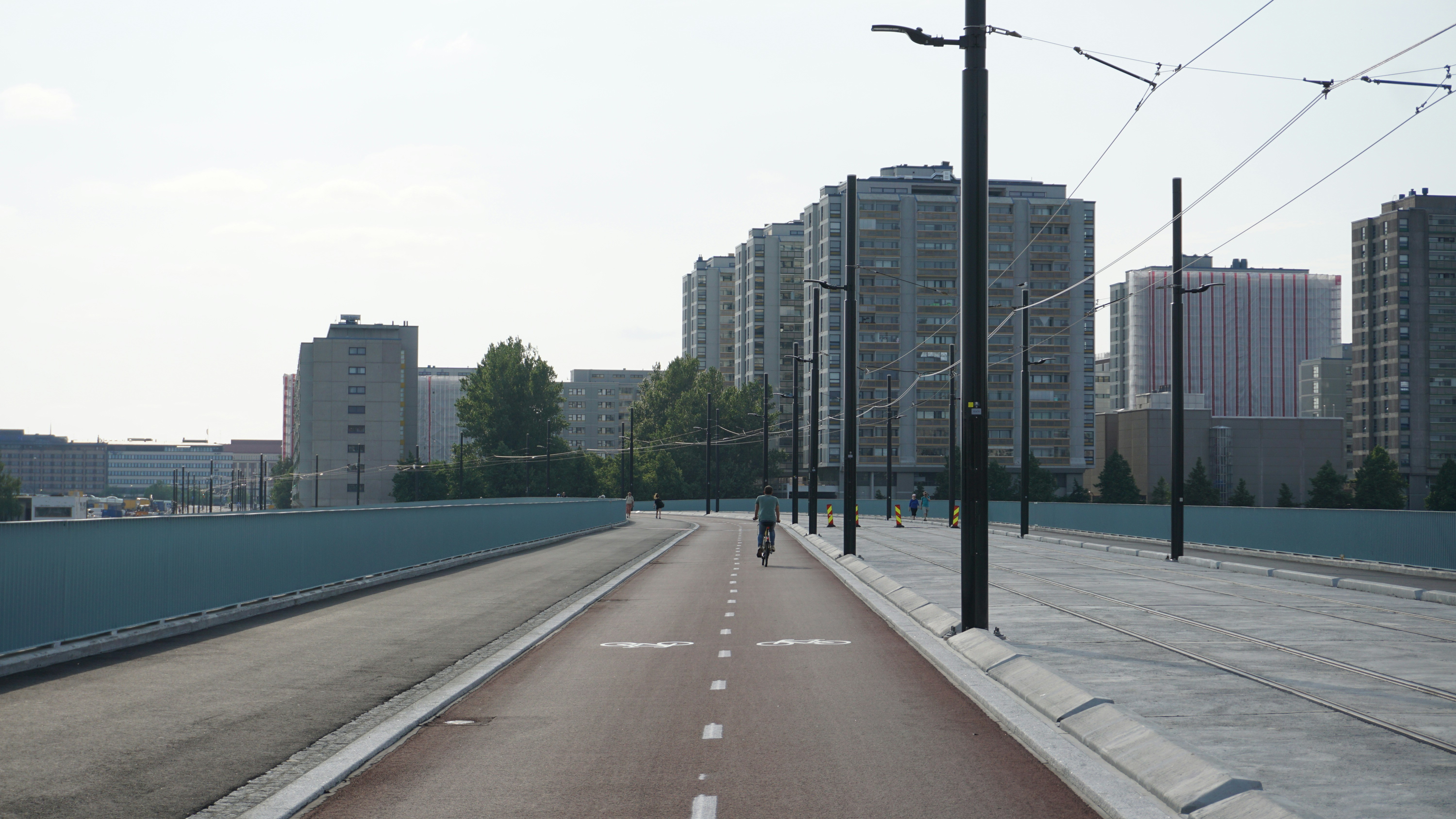 A cyclist rides on a red bike path with buildings ahead.