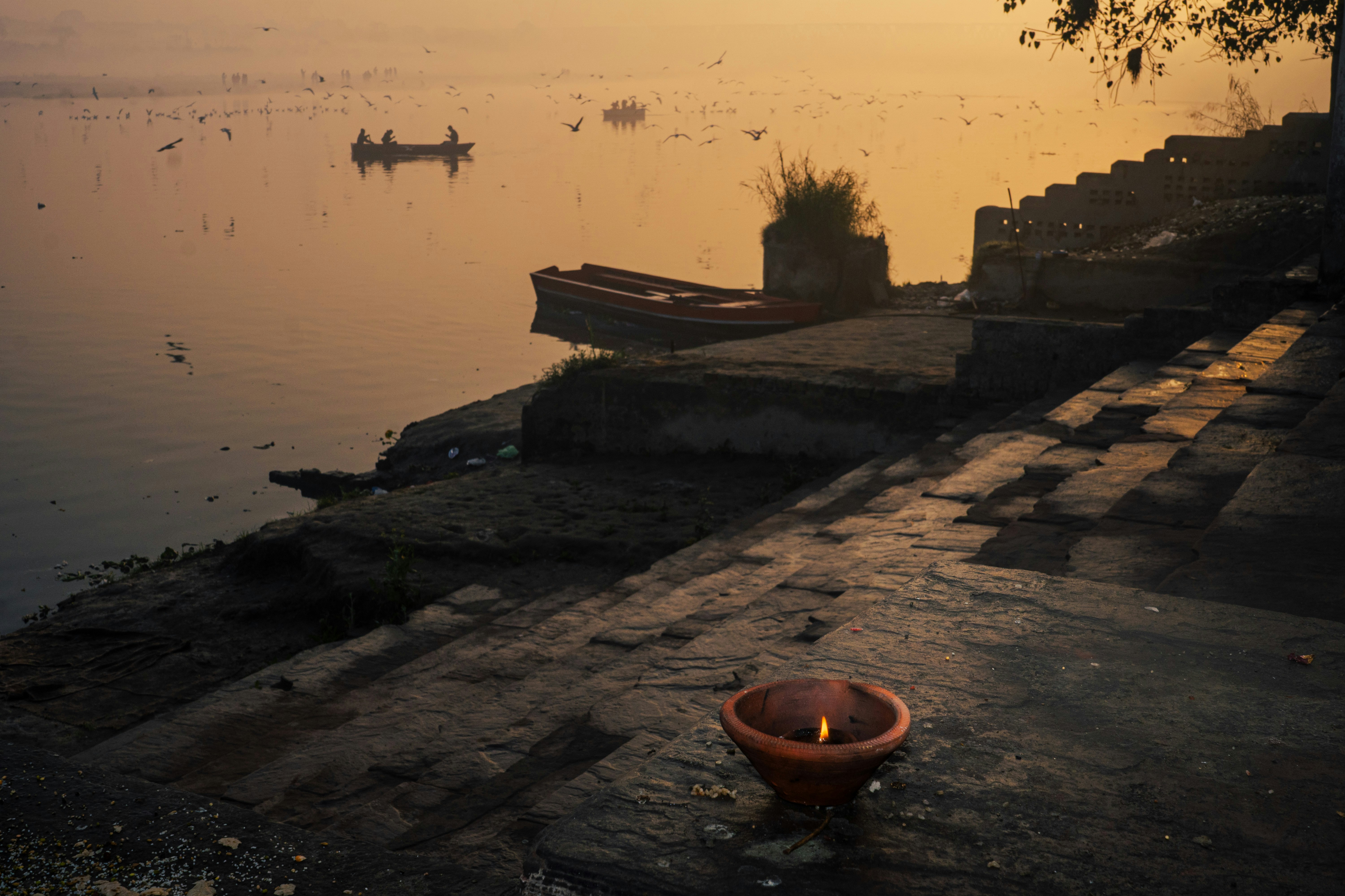 Steps leading to a river at sunrise with boats.