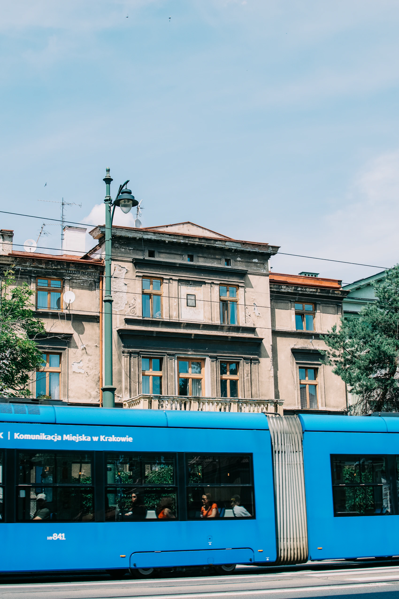 A blue Kraków tram passing weathered historic buildings on a clear day