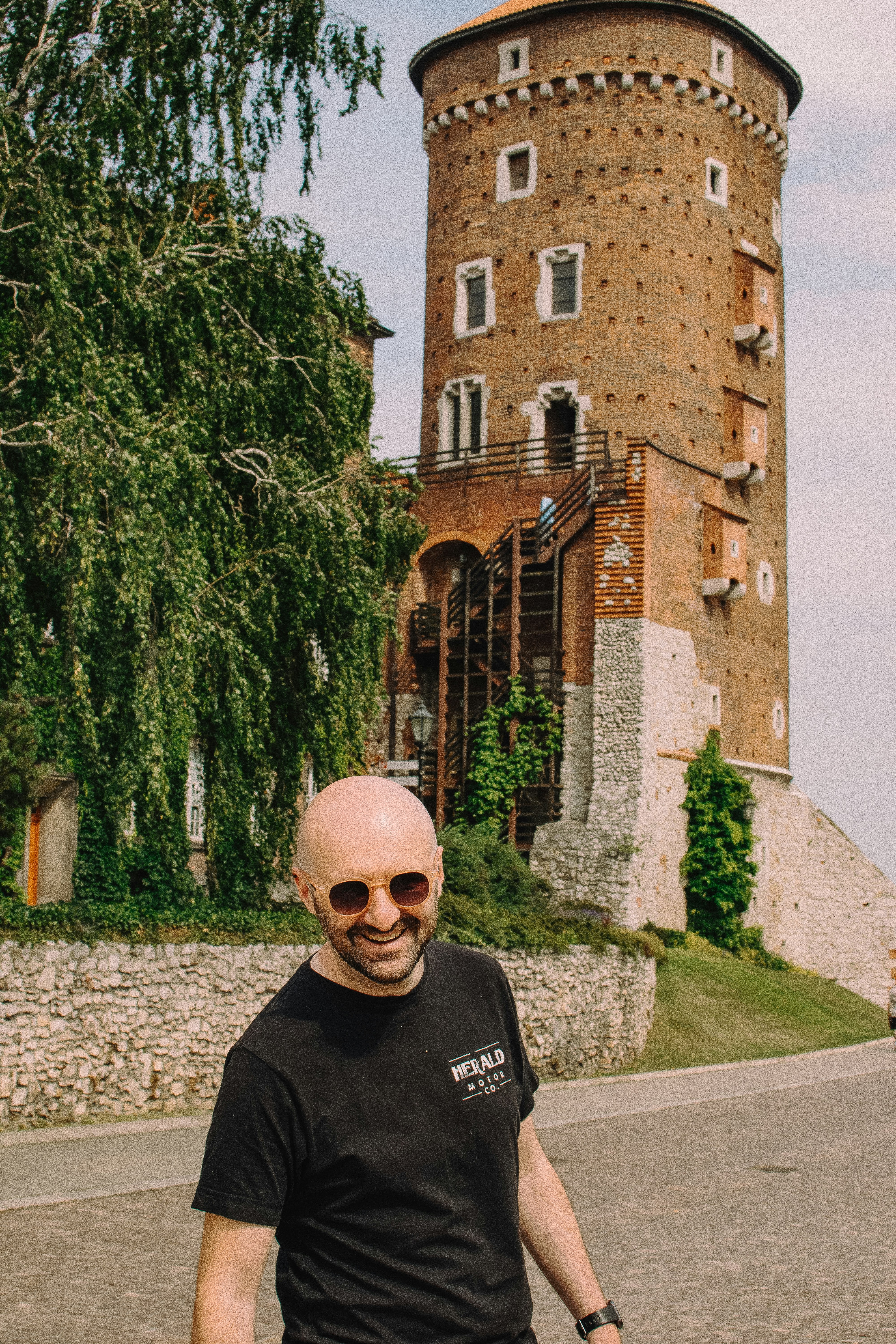 Bald man with sunglasses smiles near a brick tower.