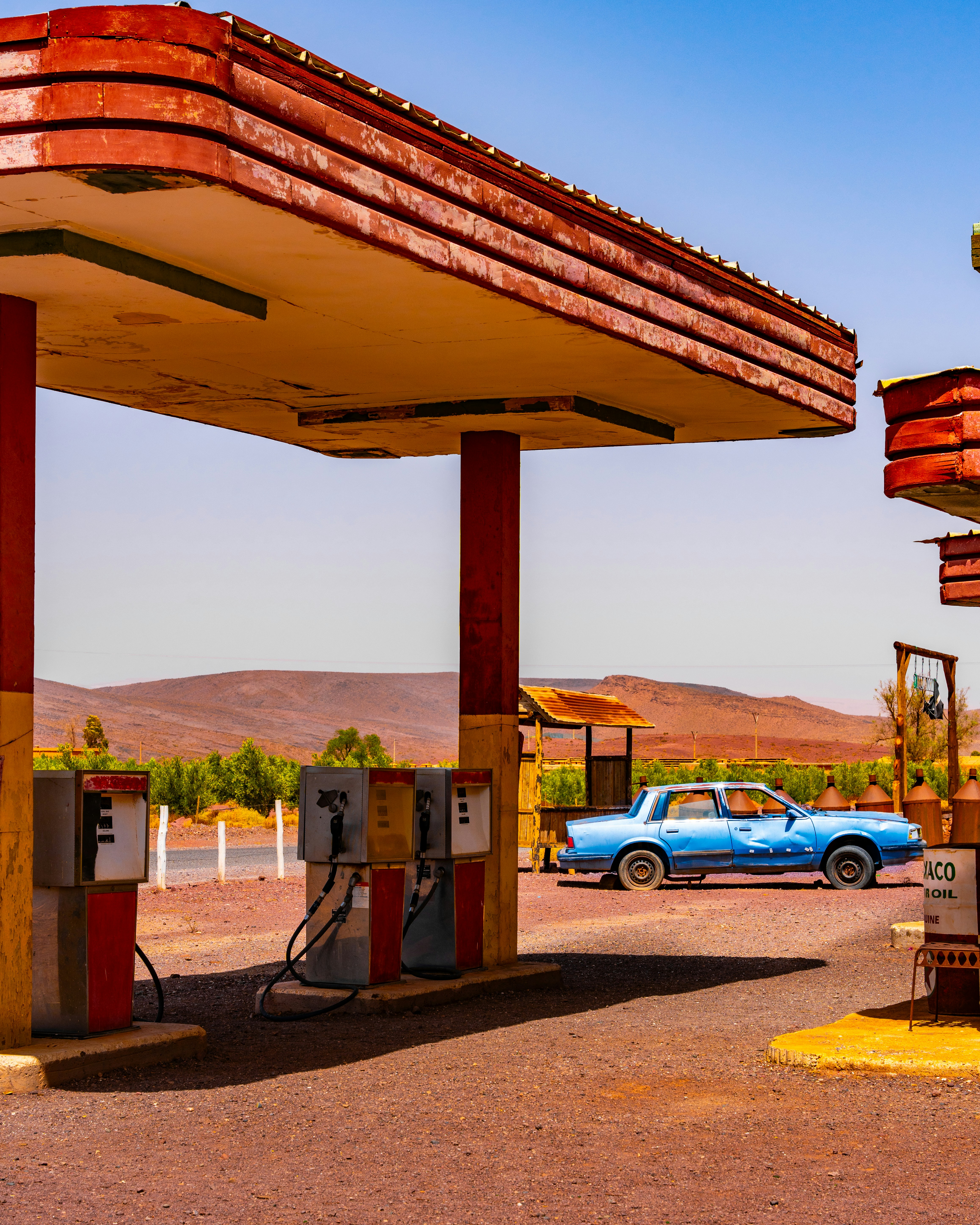 Pom bensin gurun yang ditinggalkan dengan mobil biru vintage.