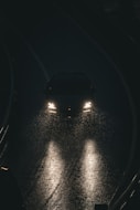Car headlights illuminate a wet road at night