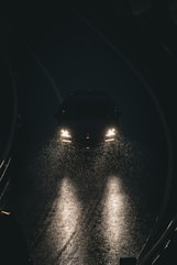 Car headlights illuminate a wet road at night