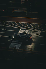 A black car drives on a wet street at night.