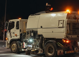 Street sweeper truck operating at night with lights on.