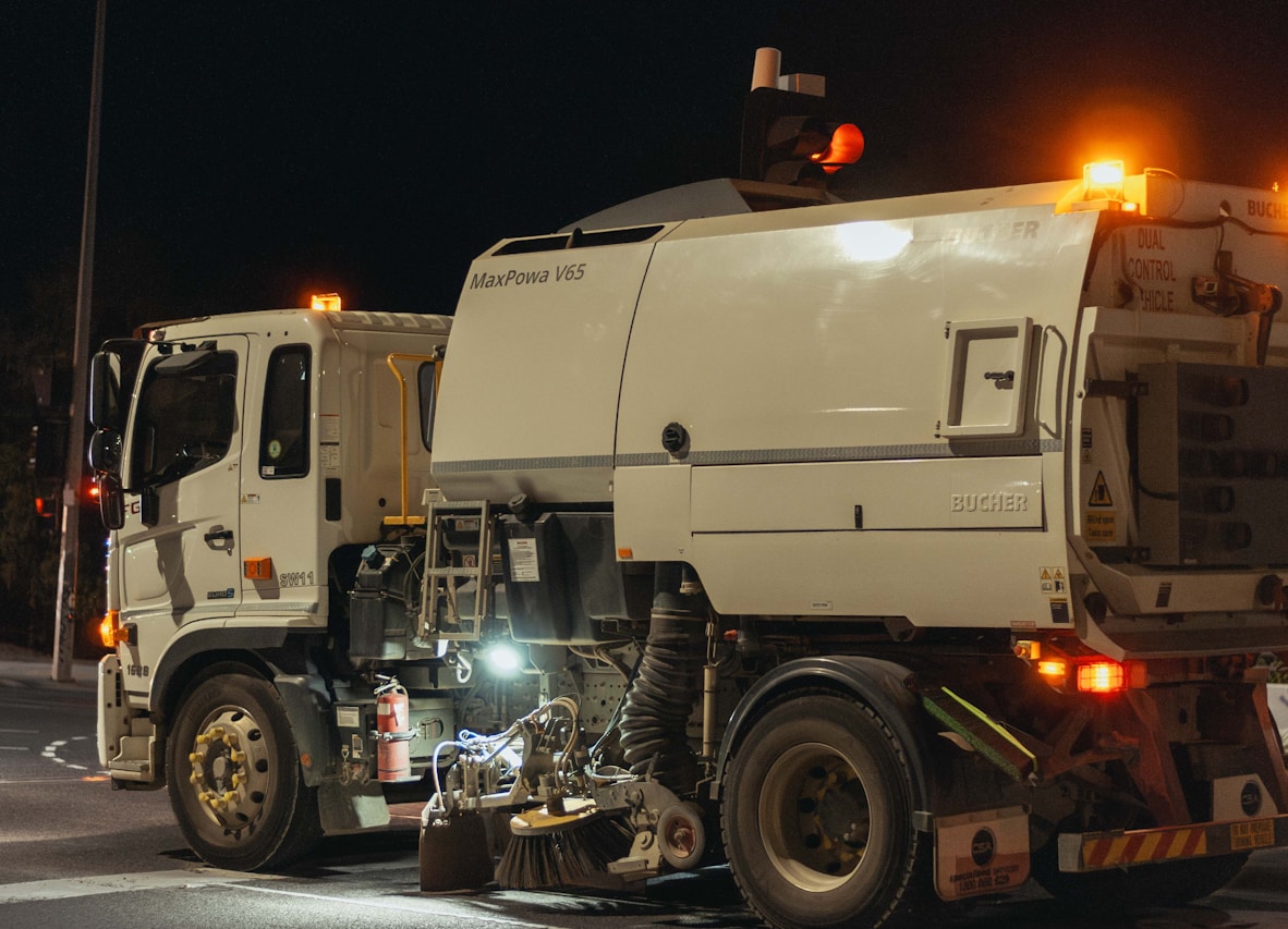 Street sweeper truck operating at night with lights on.