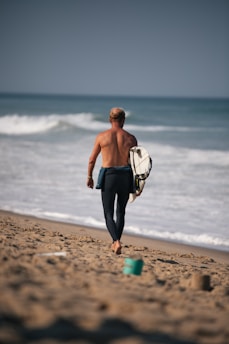 Surfer walking on beach towards ocean waves