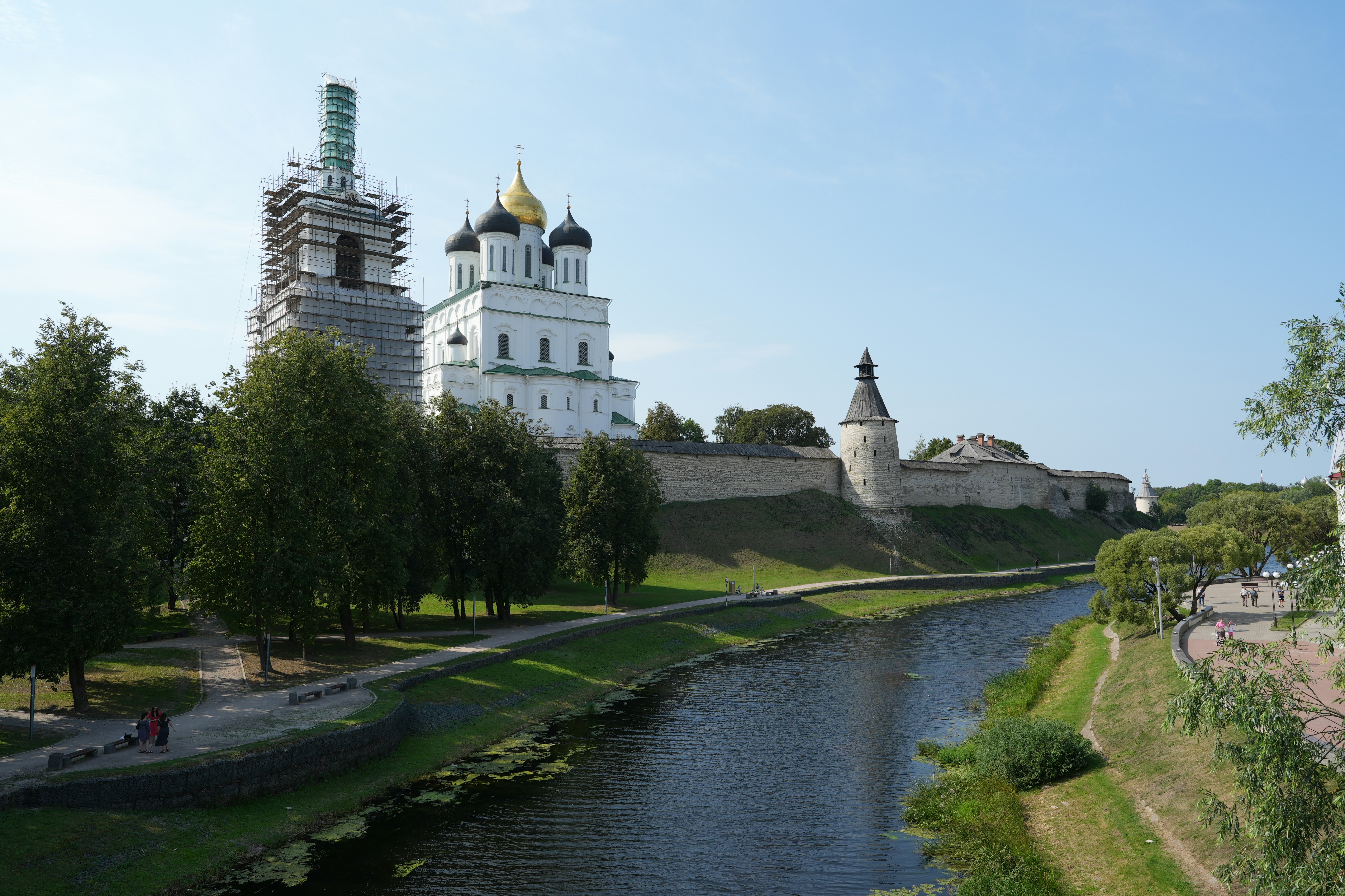 White church with golden domes beside river and trees