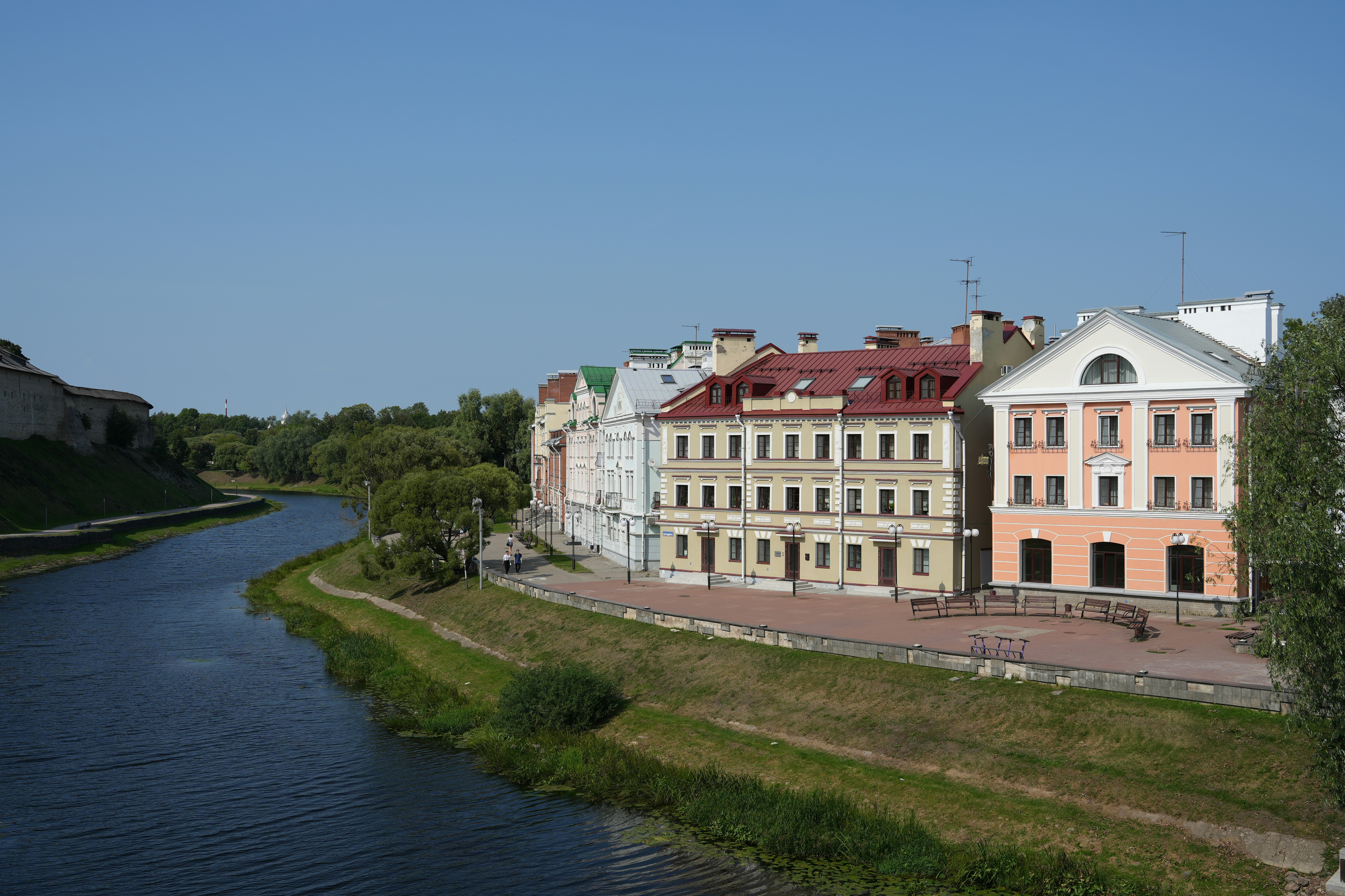 Buildings line a riverbank under a clear blue sky.