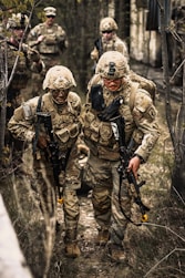 Soldiers in camouflage gear walking through a wooded area.