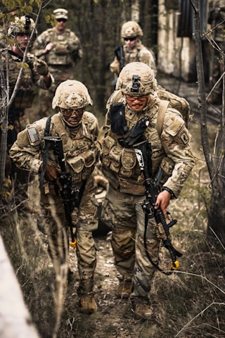 Soldiers in camouflage gear walking through a wooded area.