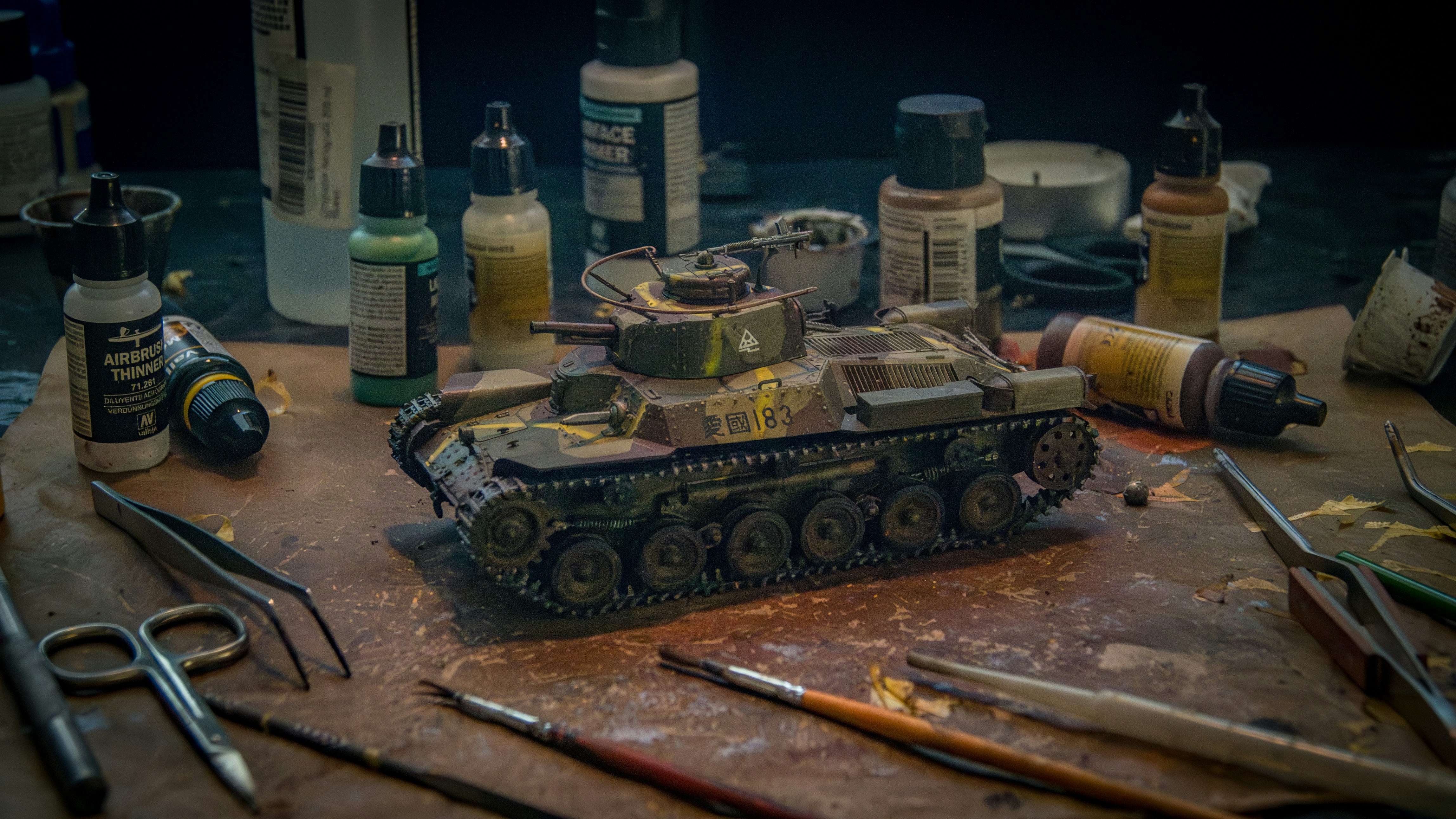 Model tank surrounded by hobby tools and paints.