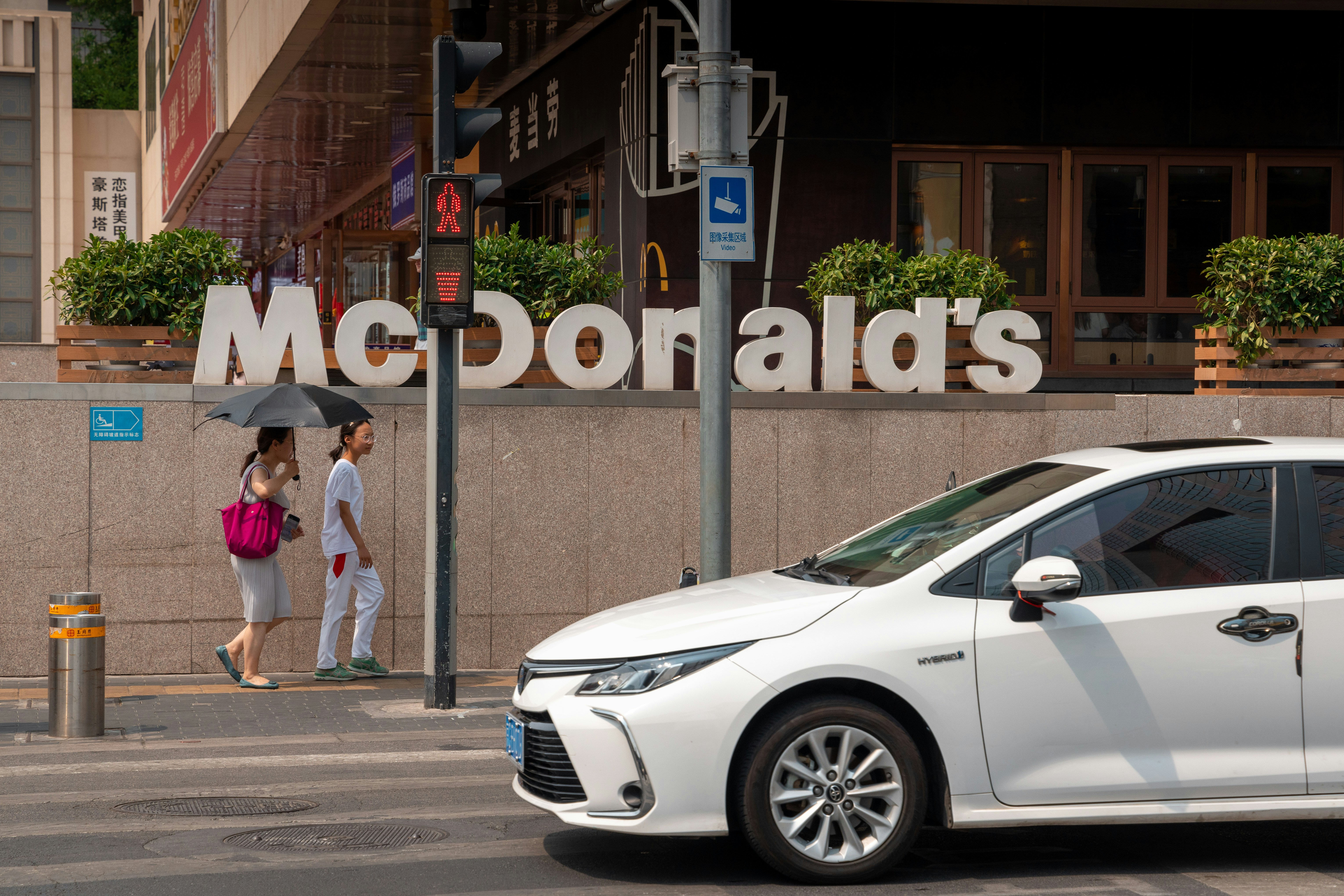 White car drives past mcdonald's with pedestrians