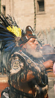 Man in traditional headdress blowing smoke from bowl