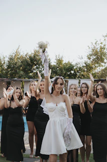 Bride holds bouquet, bridesmaids clap in black dresses