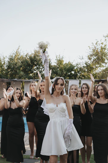 Bride holds bouquet, bridesmaids clap in black dresses