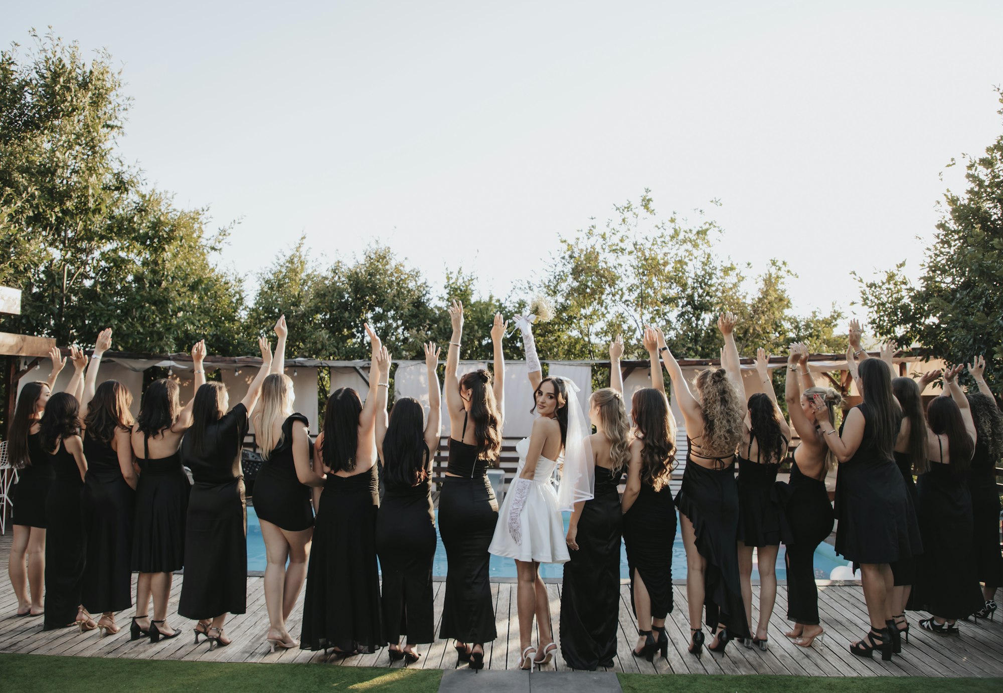 Bride and bridesmaids celebrating with raised arms in an outdoor garden setting, filled with laughter and joy