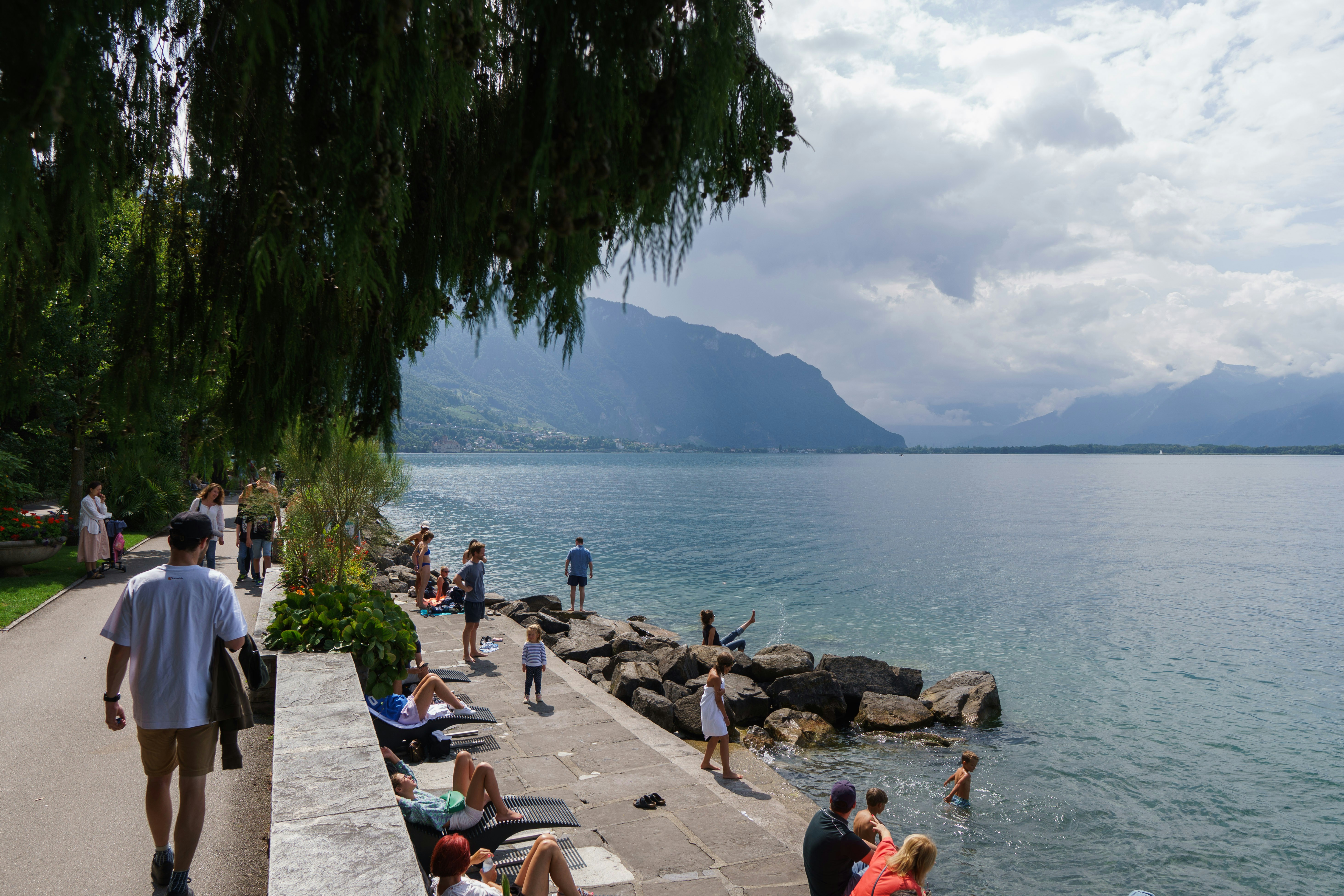 People relax by a lake with mountains in the background.