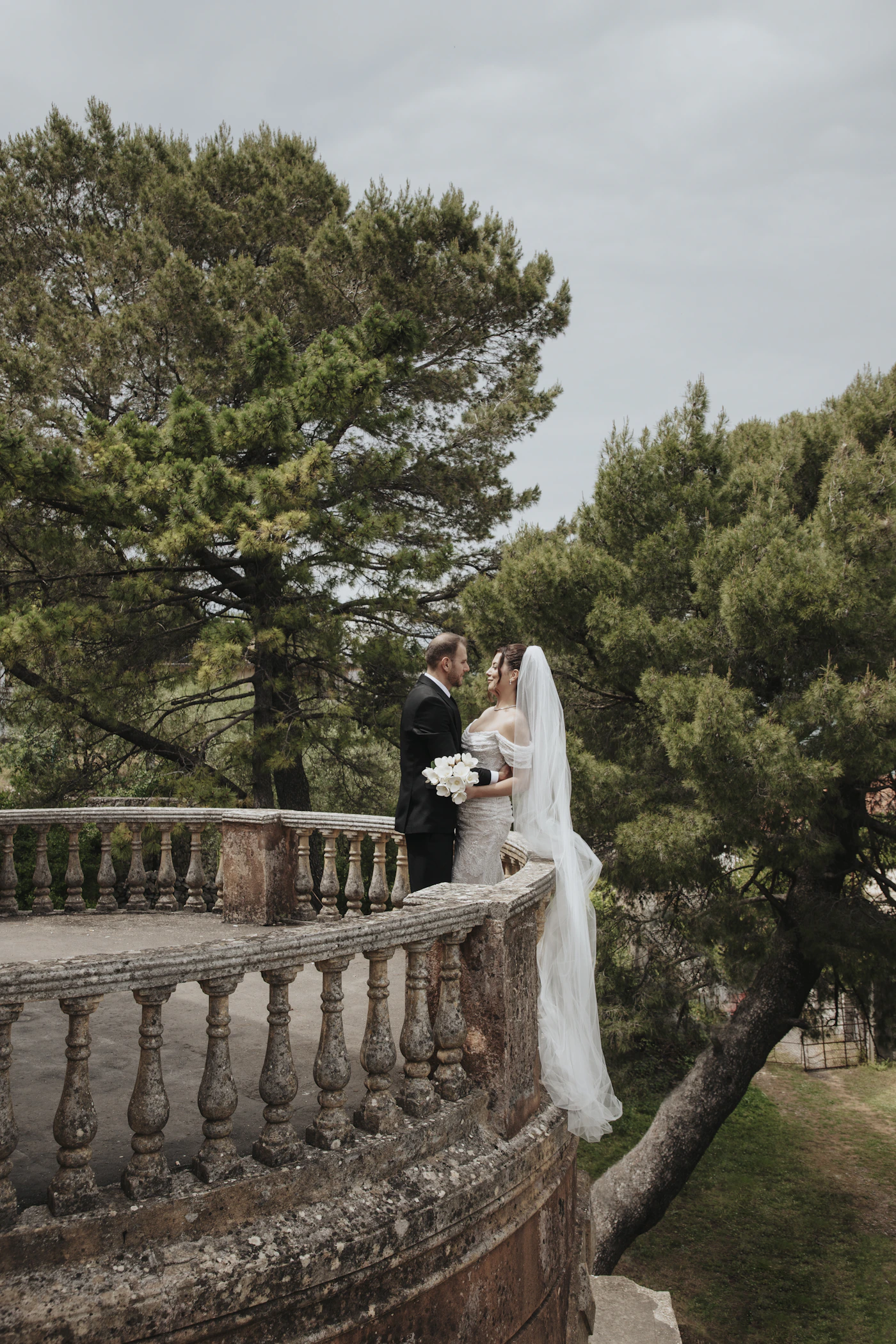 Couple in wedding attire embracing on a historic stone balcony