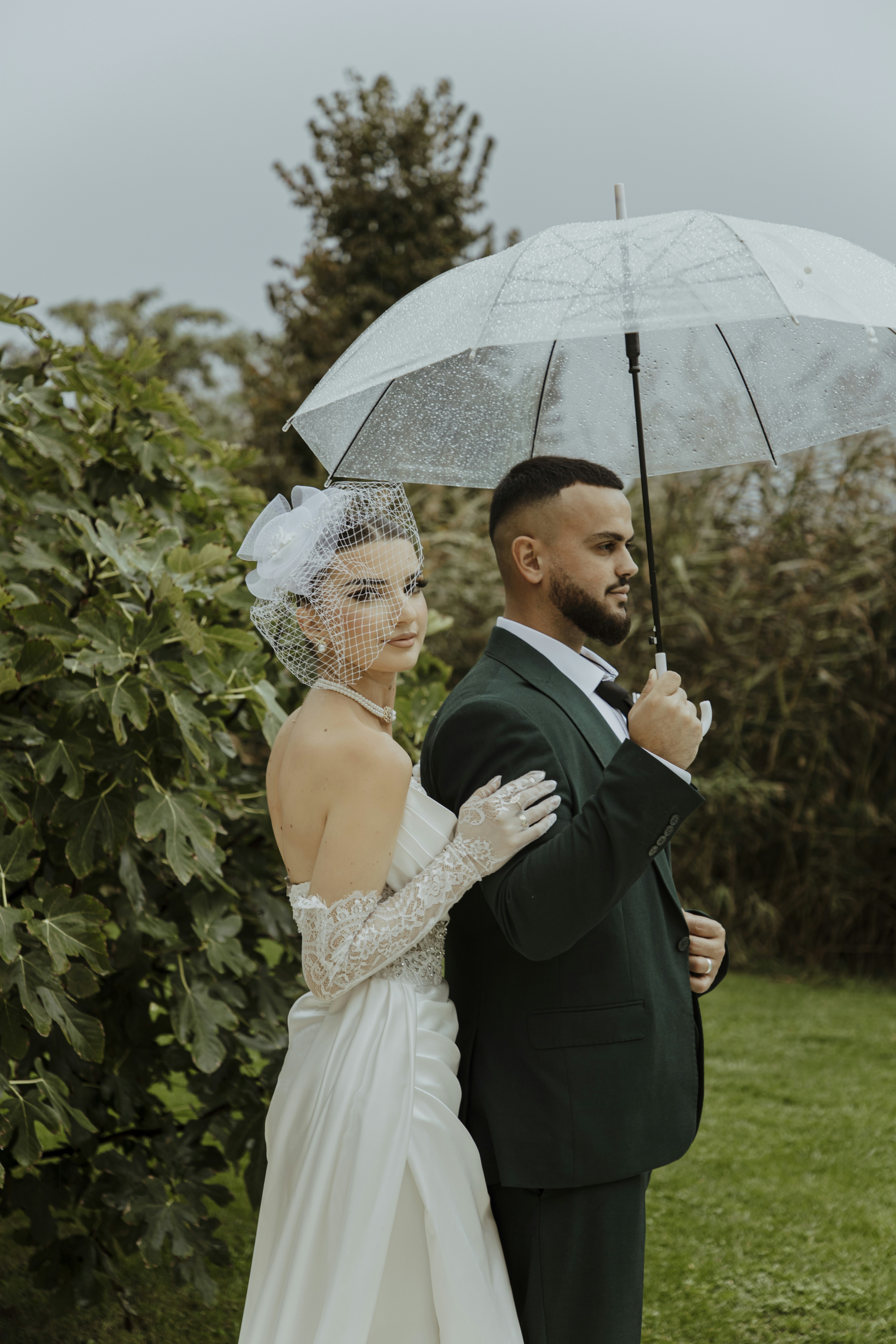Bride and groom share an umbrella on a rainy day.