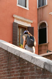 Woman with backpack climbs stone stairs near building.