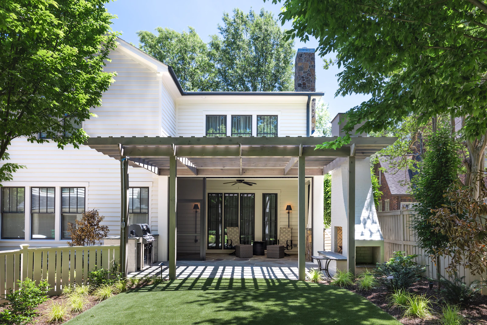 A white two-story home with a covered pergola patio and a green lawn