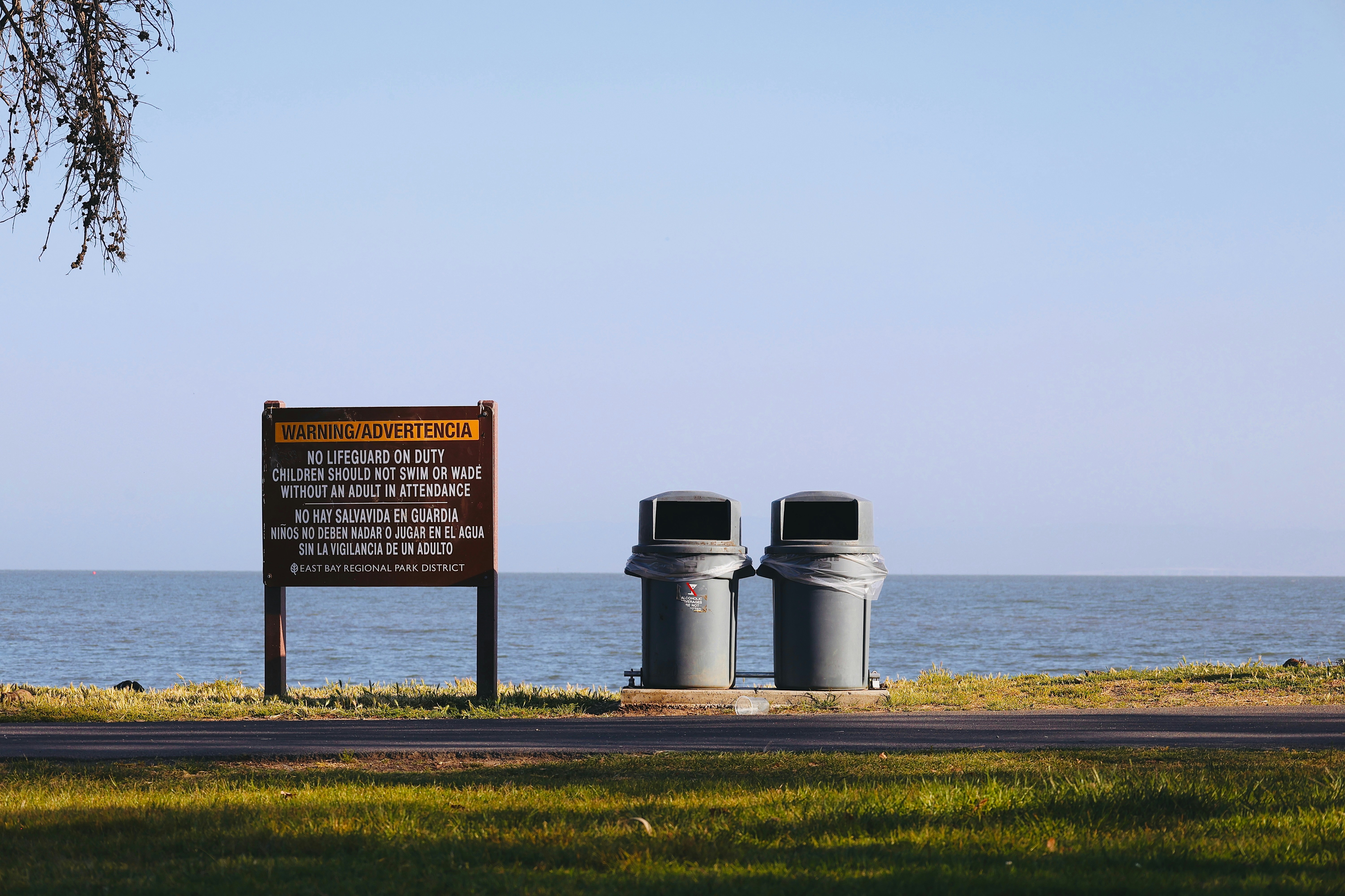 Sign and trash cans by the calm ocean.