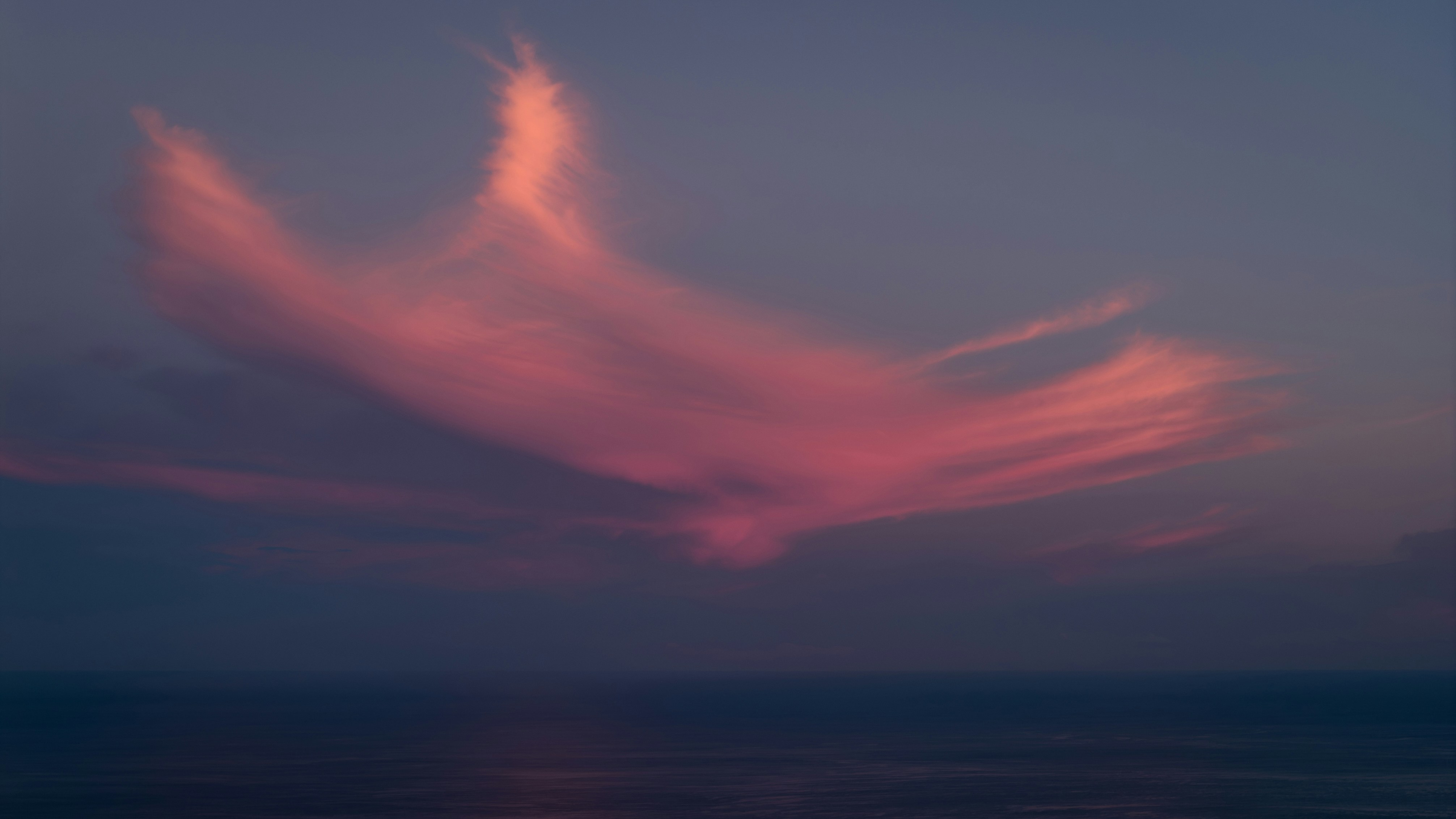 Des nuages roses dérivent au-dessus de l’océan au crépuscule