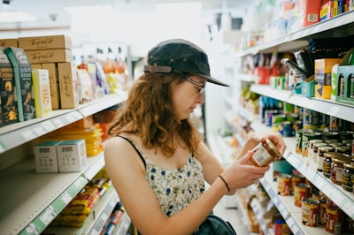 Woman reads label on jar in grocery store aisle.