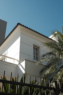 White building corner with palm trees and fence