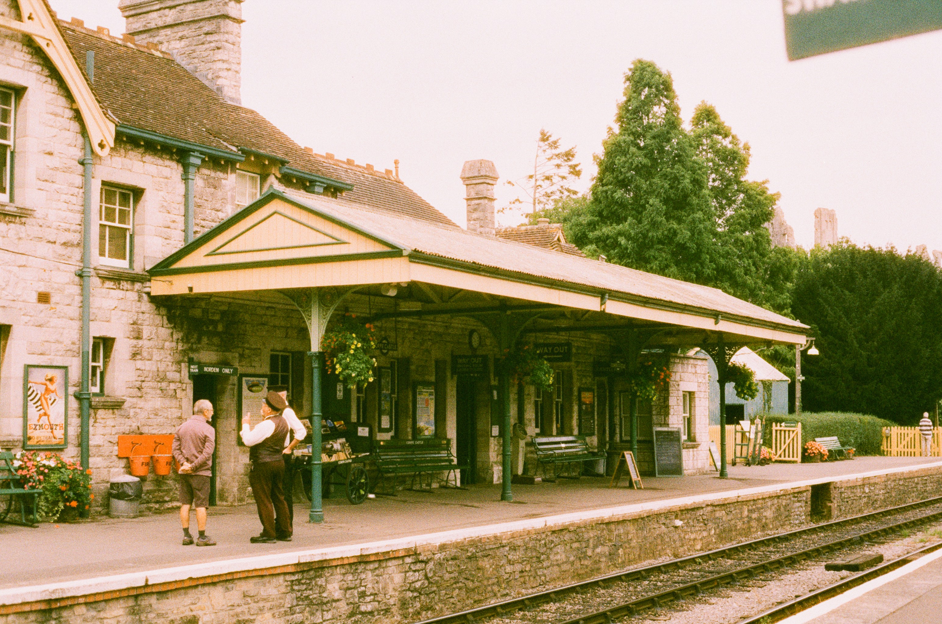 Two people stand on a vintage train station platform.