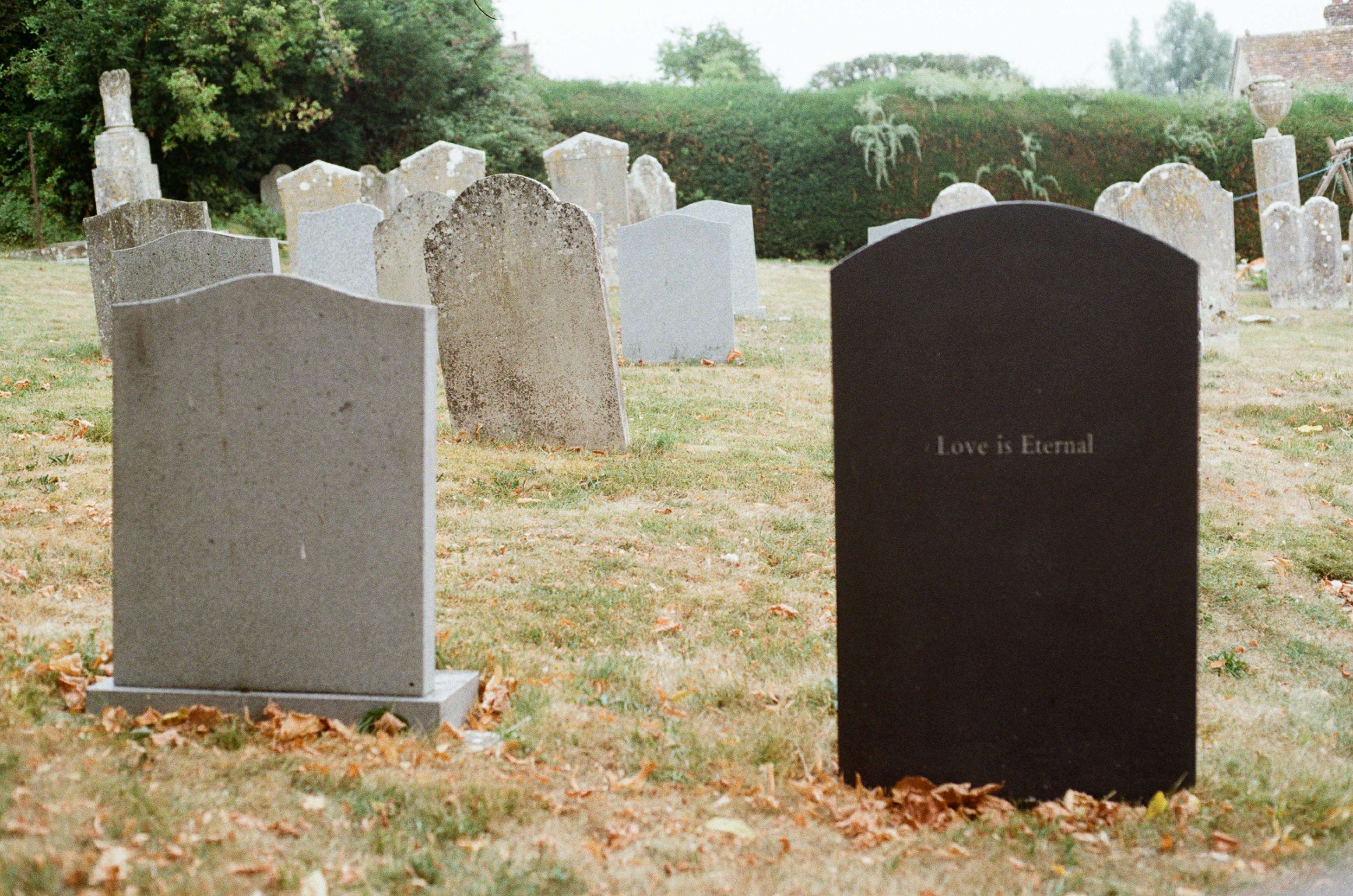 Two gravestones stand in a grassy cemetery