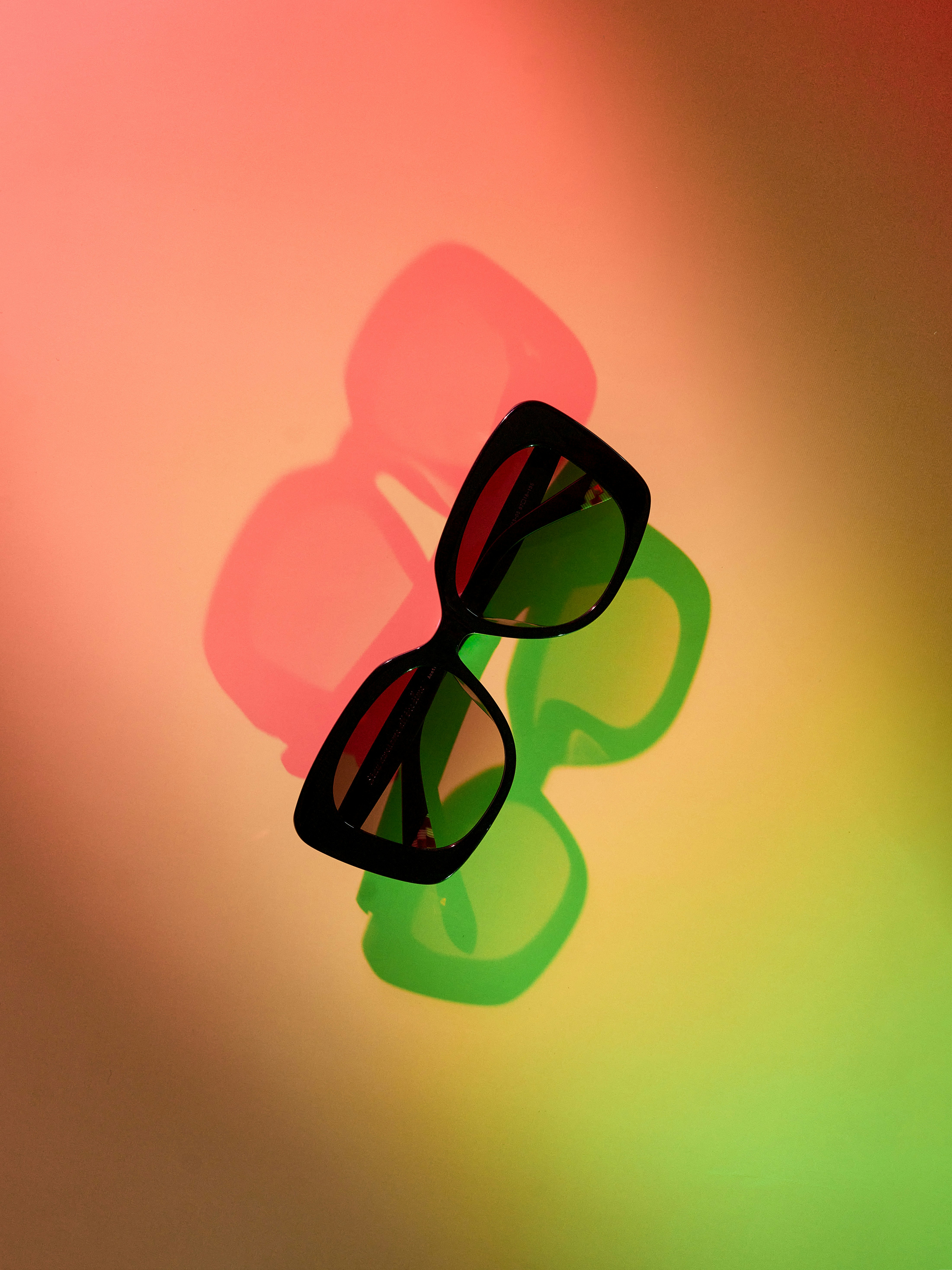 Stylish sunglasses casting colorful shadows on a gradient background.