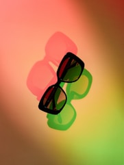 Stylish sunglasses casting colorful shadows on a gradient background.