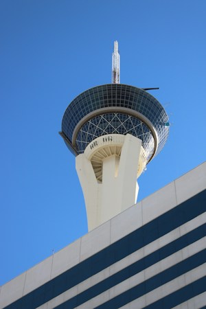A modern glass skyscraper with an observation level seen against a clear blue sky