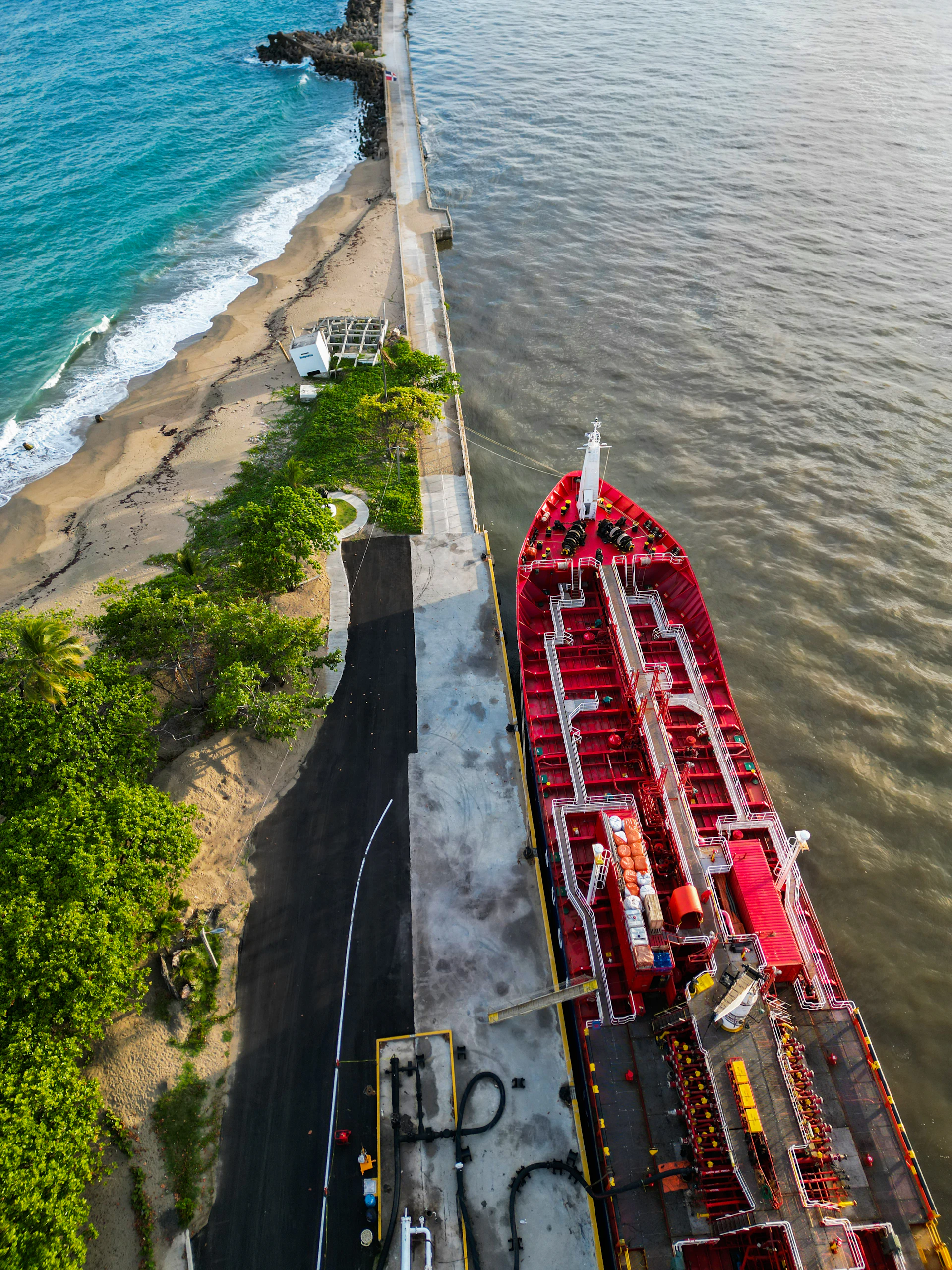 Red tanker ship docked at a pier with ocean waves