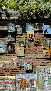 Various paintings from Georgia displayed on a brick wall.