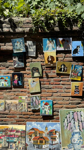 Various paintings from Georgia displayed on a brick wall.