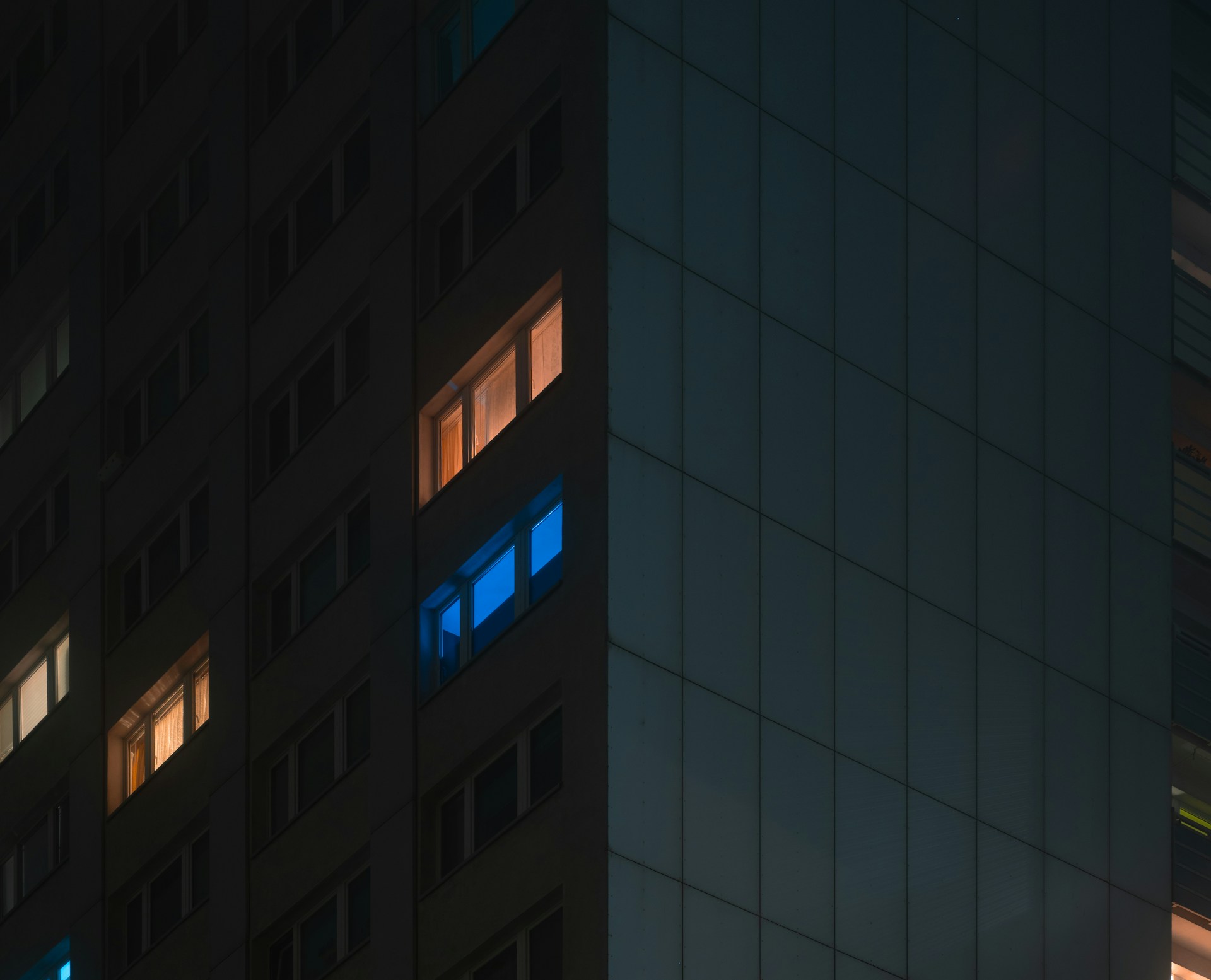 Tall apartment building at night with glowing windows.