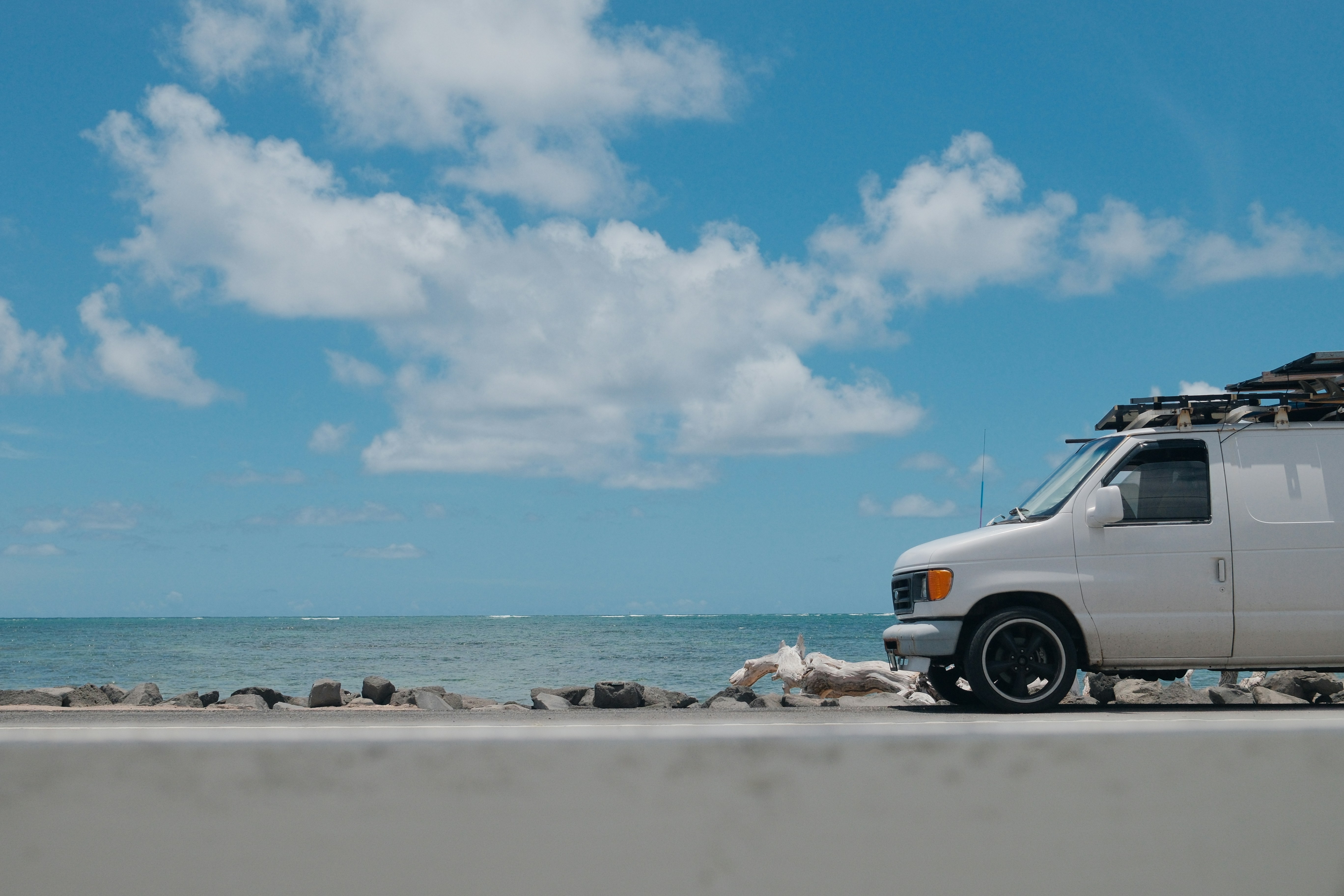 Camioneta blanca estacionada junto al océano bajo un cielo azul.
